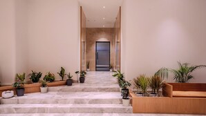 Un hall d’hôtel moderne avec un escalier en marbre, des plantes en pot et un banc en bois.
