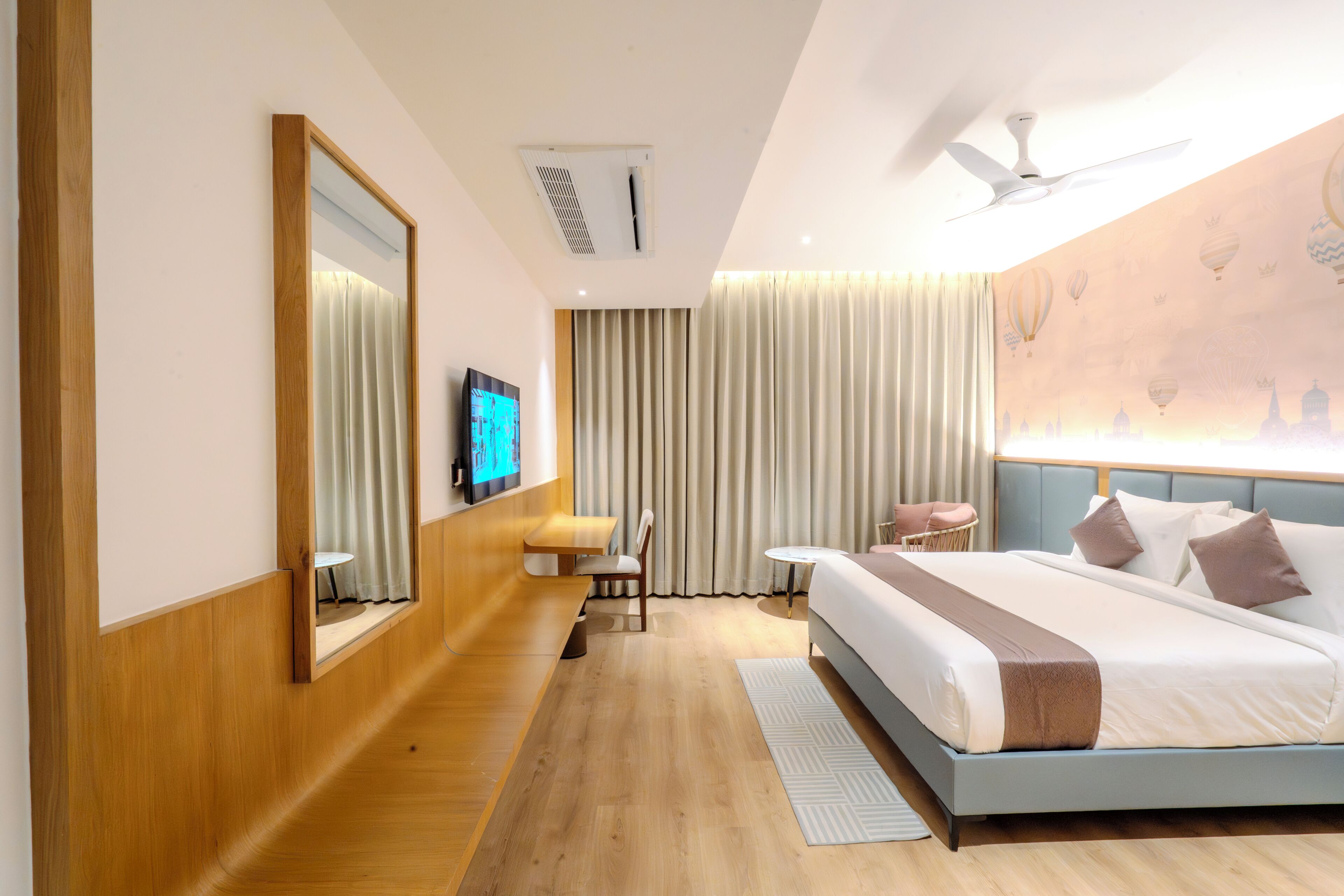 A hotel room with a bed, a TV, a ceiling fan, and a large window with curtains.