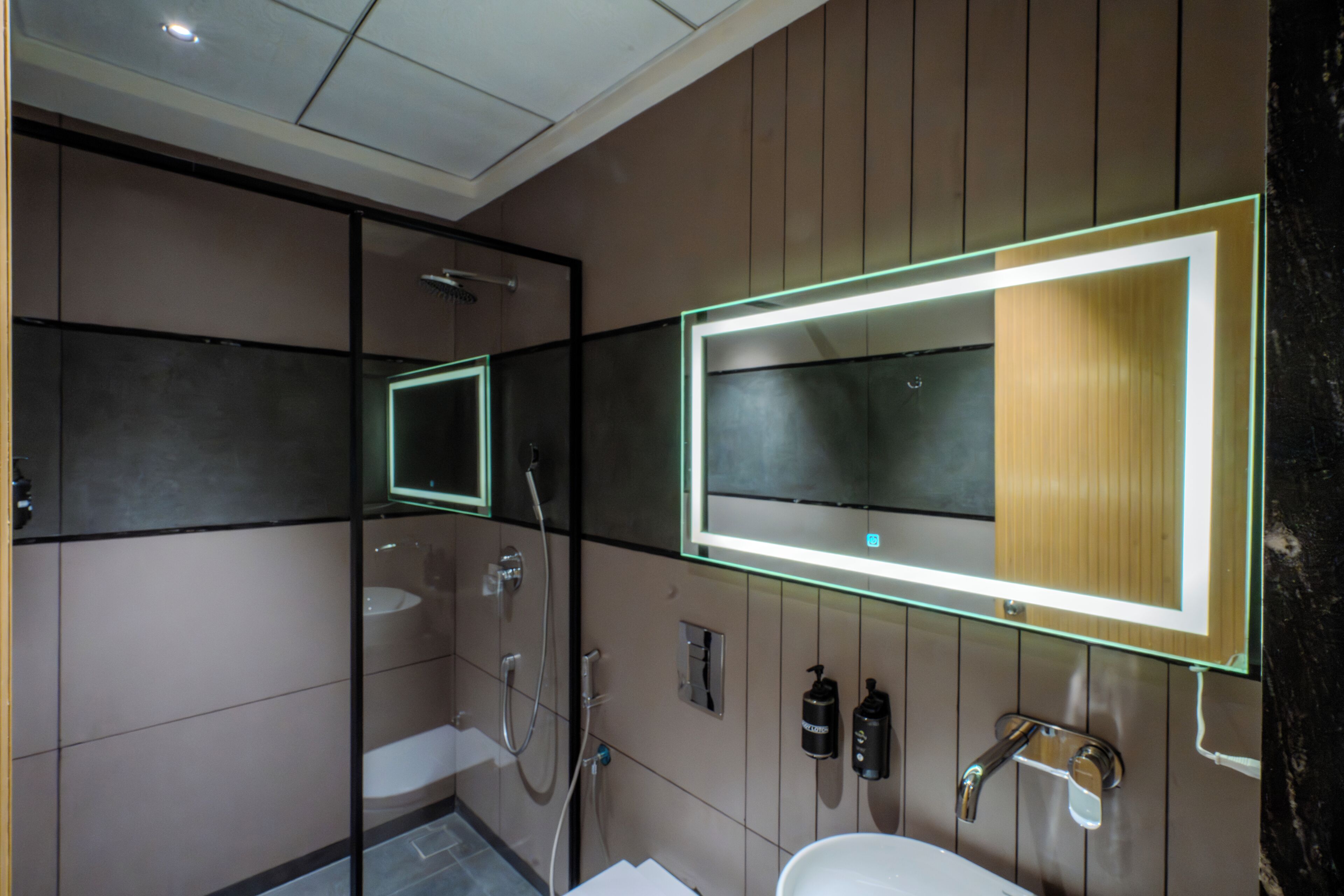 Une salle de bain moderne avec une douche à parois de verre, un grand miroir doté d’un éclairage à DEL et un lavabo blanc.