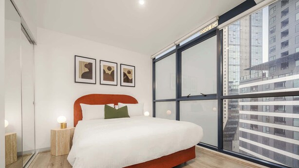 A modern bedroom with a large window, a bed with a red headboard, and three framed pictures on the wall. - LaneStay - 2BR in Southbank w Large Living and Gym (Southbank)