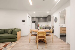 A modern living room with a green sofa, a dining table with four chairs, a kitchen area with cabinets and appliances, and a bathroom with a mirror and sink. - LaneStay - 2BR in Southbank w Large Living and Gym (Southbank)