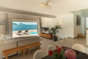 A modern living room with a sofa, a dining table, a TV, and a potted plant. - Casa del Mar -beautiful house vilt pool ans spectacular sea views to Es Vedra (Balearic Islands)