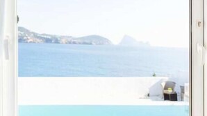 Quarto com uma janela grande que dá para uma piscina e vista para o mar.