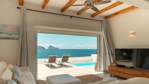 Quarto com uma cama grande, televisão, ventoinha no teto e vista para o mar.