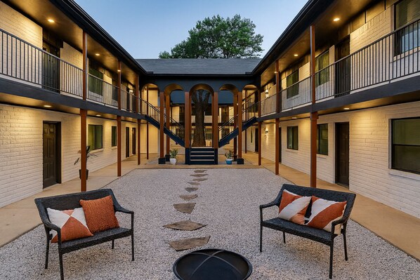 A courtyard with two outdoor seating areas, a central staircase, and a building with multiple balconies and windows.