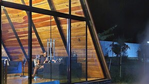 A modern, triangular wooden structure with large windows and a fire pit outside.