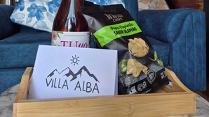 A bottle of wine, a bag of chips, and a card on a tray in a room with a wooden ceiling and a blue couch.