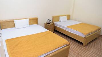 Two single beds with wooden headboards, a nightstand with a kettle, and a plain wall.