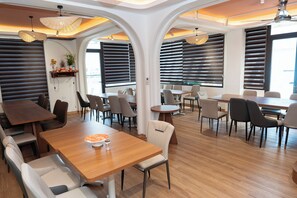 A spacious dining area with multiple tables and chairs, large windows with blinds, and a ceiling with recessed lighting. - 12 Ao Ca Hotel (Bai Chay)