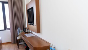 Habitación de hotel con escritorio de madera, televisor montado en la pared, una silla, una mesita con bandeja y una ventana con cortinas.