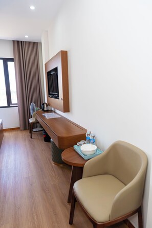 Habitación de hotel con escritorio de madera, televisor montado en la pared, una silla, una mesita con bandeja y una ventana con cortinas.