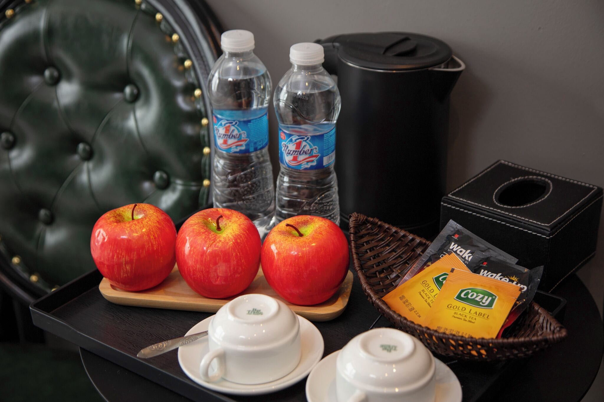 A tray with apples, water bottles, a coffee maker, and tea bags.