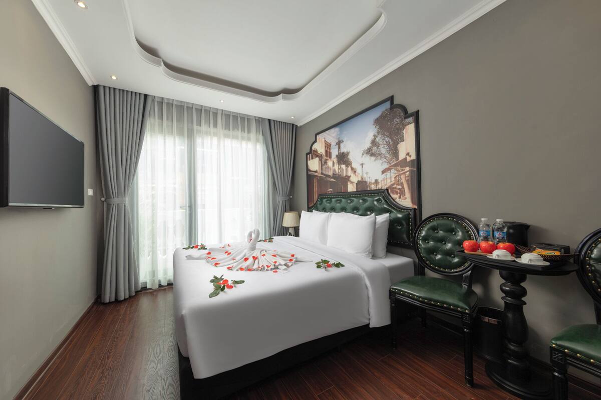 A hotel room with a large bed, a television, a table with a tray, and a painting on the wall.