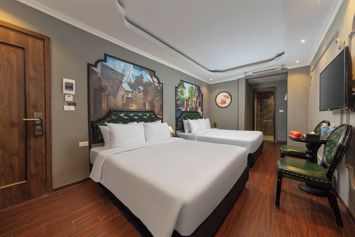 A hotel room with two beds, a wooden door, a flat-screen TV, and artwork on the walls.