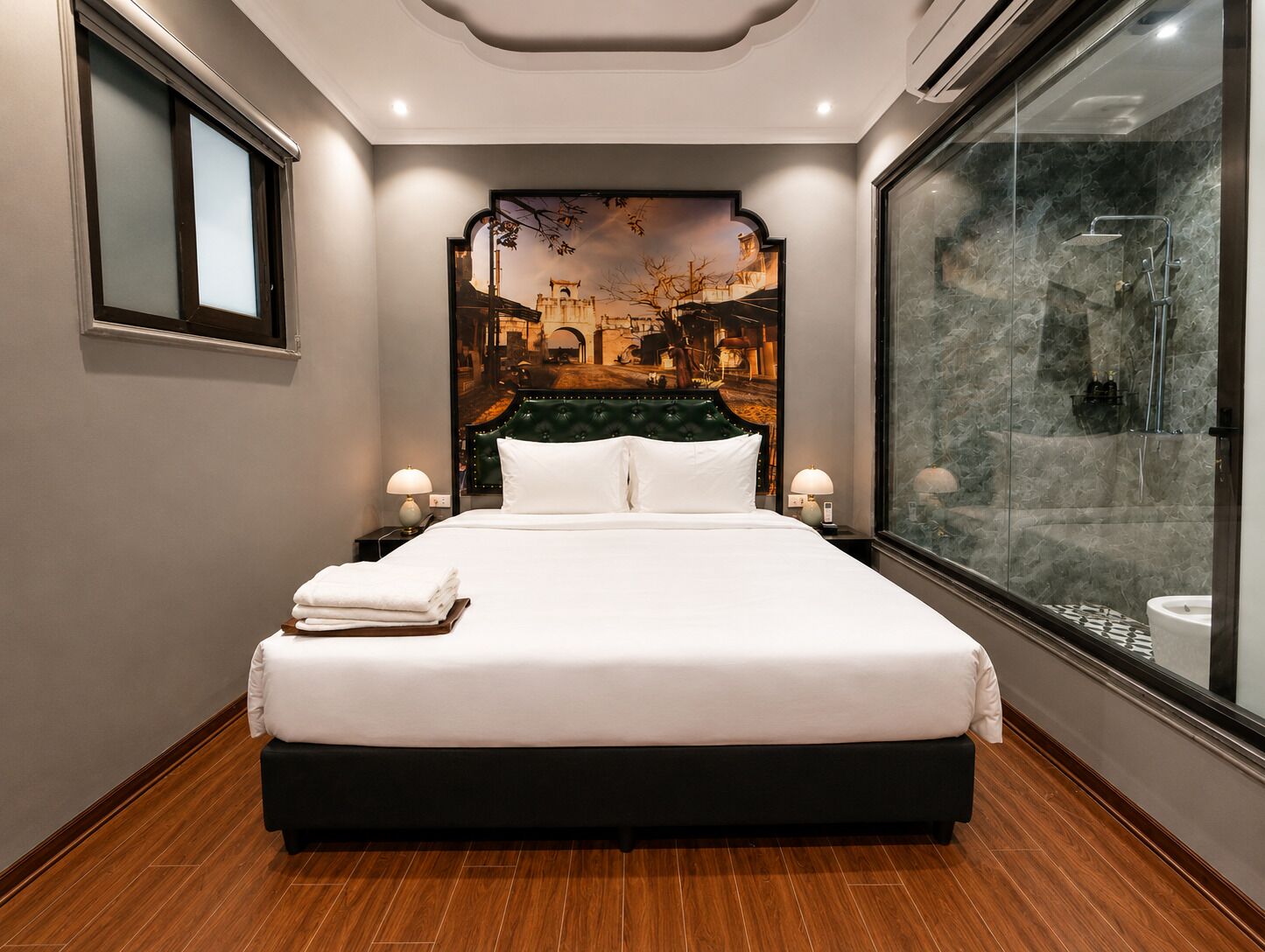 A hotel room with a large bed, a headboard with a cityscape mural, a glass shower enclosure, and a wooden floor.