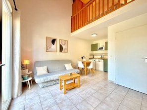 A living room with a sofa, a wooden coffee table, a dining table with chairs, a kitchen area with a microwave, and a door. - Le Nid du Mas, 2 pers pool in Calvisson (Calvisson)