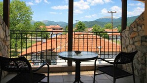 A balcony with a round table and two chairs, a stone wall, and a view of a town with red-roofed buildings and green hills. - Ducata Hotel - Single Room With Balcony Views (Veroia)