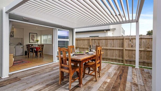 A wooden deck with a table and chairs, a pergola, and a view of a backyard. - Aiturangi Retreat Whangamata (Whangamata)