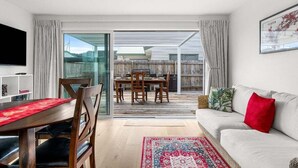 A modern living room with a dining area, a sofa, and a TV. - Aiturangi Retreat Whangamata (Whangamata)