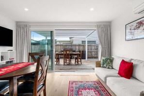 A modern living room with a dining area, a sofa, and a TV. - Aiturangi Retreat Whangamata (Whangamata)