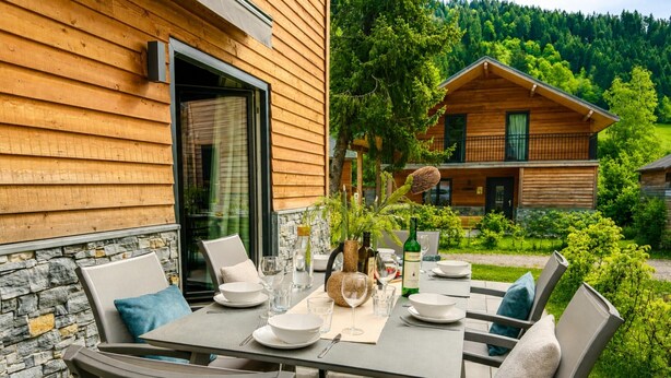 Una baita di legno con zona pranzo, un tavolo apparecchiato per quattro persone, posti a sedere all'aperto e vista su un paesaggio boschivo.