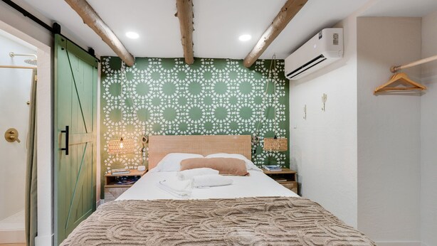A bedroom with a bed, a wooden headboard, a green patterned wall, a hanging light fixture, and a wooden door. - Bright Studio in Manitou Springs, Walk Downtown (Manitou Springs)