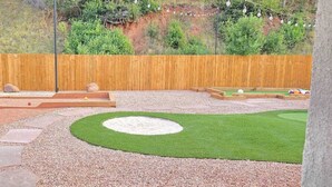 A landscaped outdoor area with a wooden fence, a circular grassy patch, and stepping stones leading to a raised platform. - Bright Studio in Manitou Springs, Walk Downtown (Manitou Springs)