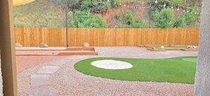 A landscaped outdoor area with a wooden fence, a circular grassy patch, and stepping stones leading to a raised platform. - Bright Studio in Manitou Springs, Walk Downtown (Manitou Springs)