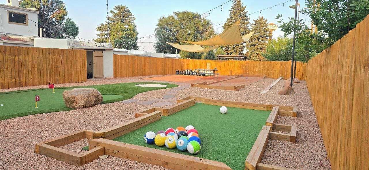 A backyard with a putting green, a sand trap, and a wooden deck.