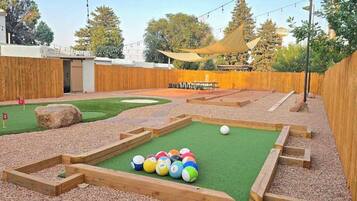 A backyard with a putting green, a sand trap, and a wooden deck.