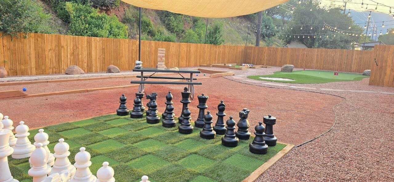 A chessboard set up on a lawn with a picnic table nearby.
