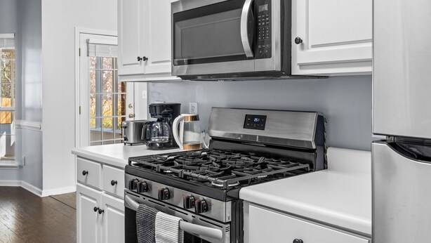 Uma cozinha com armários brancos, micro-ondas de aço inoxidável, fogão a gás e cafeteira.