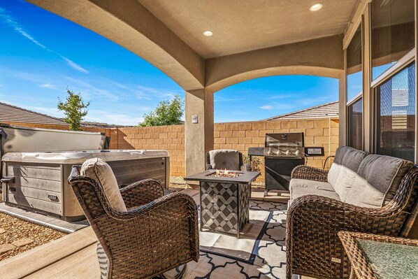 Un patio exterior con jacuzzi, parrilla y mobiliario de mimbre.