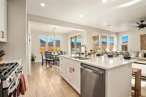 A modern kitchen with a central island, a dining area with chairs, and a view of the outside. - Paseos 1366, Ping Pong Table, Basketball Arcade, Private Hot Tub, Community Amenities! (Washington)