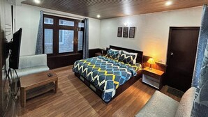 A bedroom with a bed, a desk, a chair, a TV, and a window. - Hotel Devidyar (Manali)