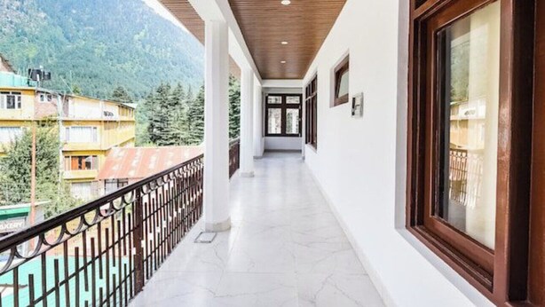A corridor with a wooden ceiling, white walls, and a balcony with a metal railing. - Hotel Devidyar (Manali)