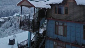 A two-story building with a balcony and a small porch, surrounded by snow-covered mountains. - Hotel Devidyar (Manali)