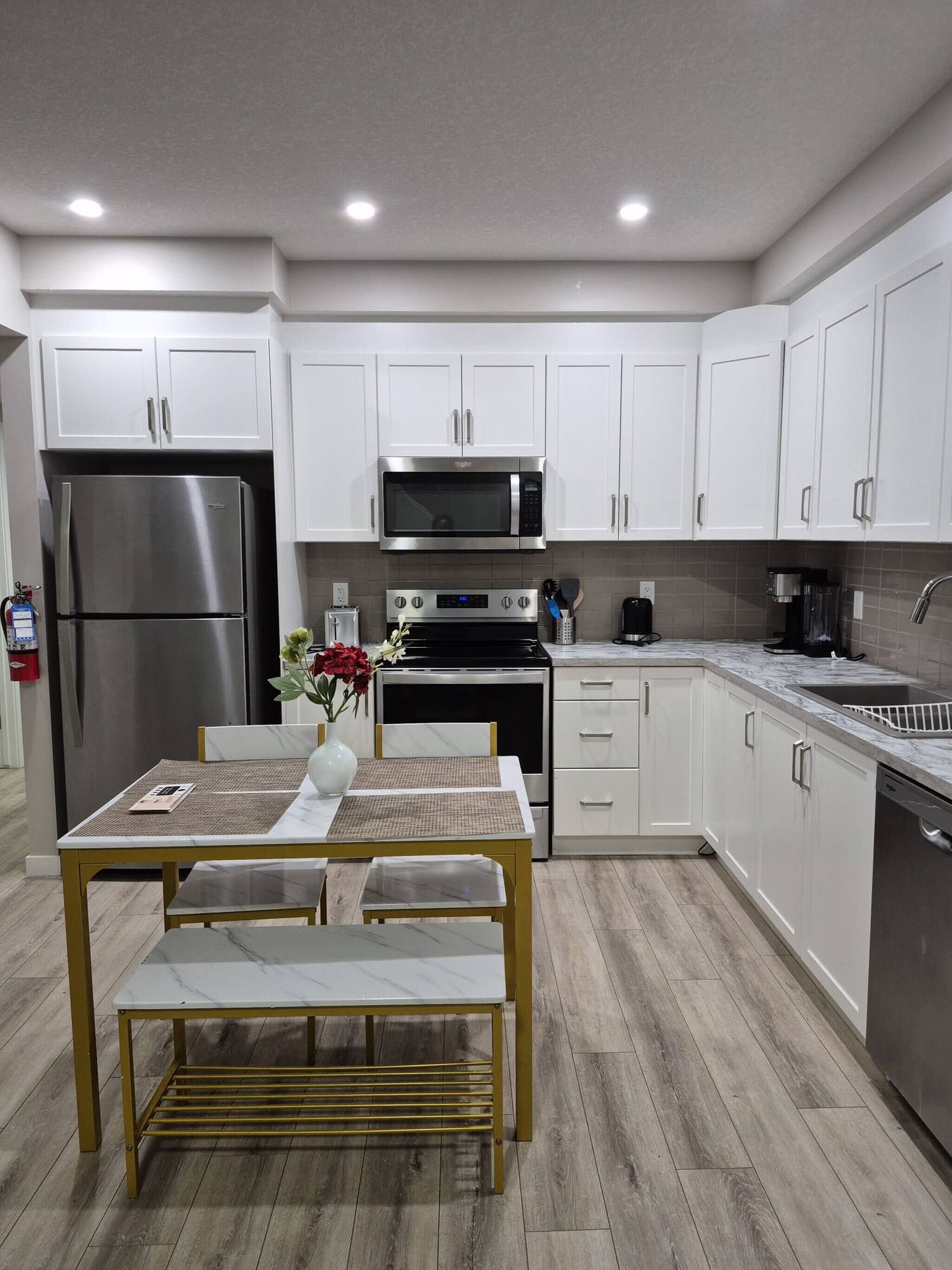 A modern kitchen with white cabinets, stainless steel appliances, and a wooden dining table with benches.