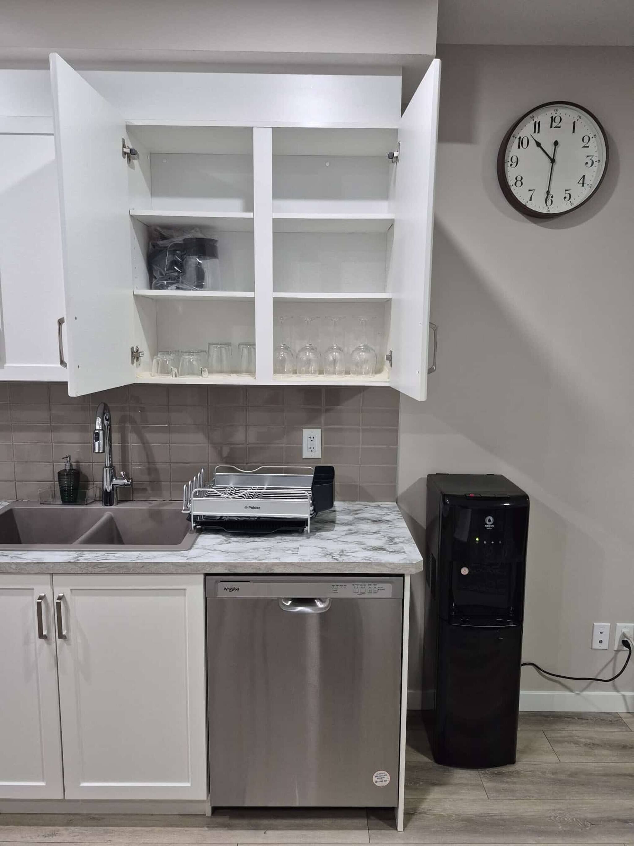 A kitchen with a dishwasher, a water dispenser, and a clock on the wall.