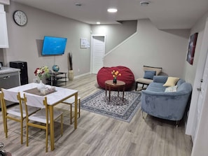 A modern living room with a dining area, a flat-screen TV, a red bean bag, a blue sofa, and a staircase leading upstairs. - A Home Away From Home (Calgary)