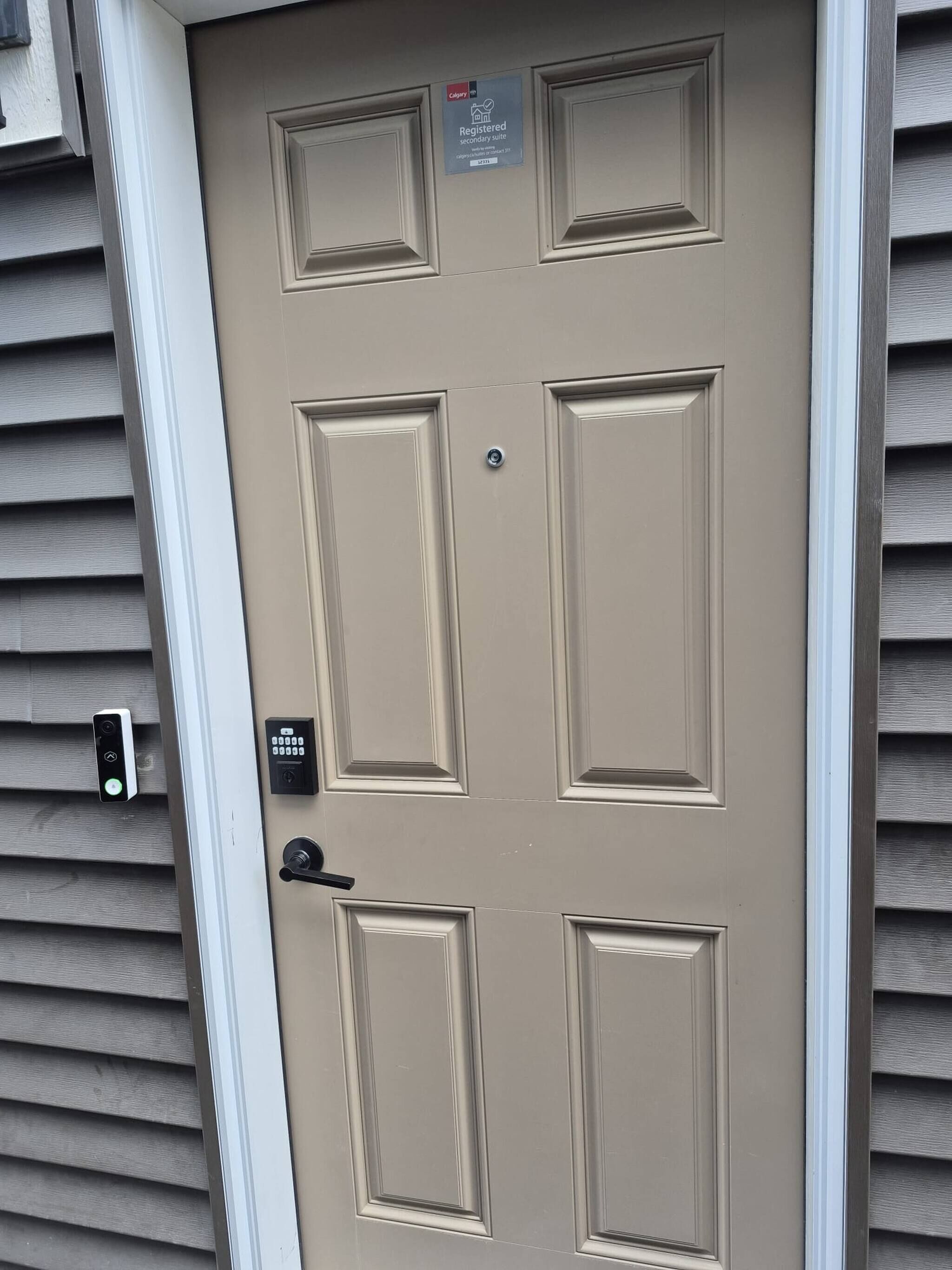 Une porte de couleur beige dotée d’un clavier pour ouvrir la porte, d’une sonnette et d’une pancarte indiquant qu’il s’agit d’un logement secondaire enregistré.