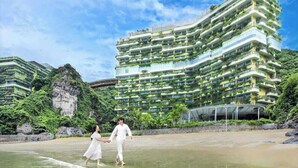 A multi-story hotel with balconies, a beach in the foreground, and greenery around. - Forest Sky Villa - Flamingo Cat Ba (Hai Phong)