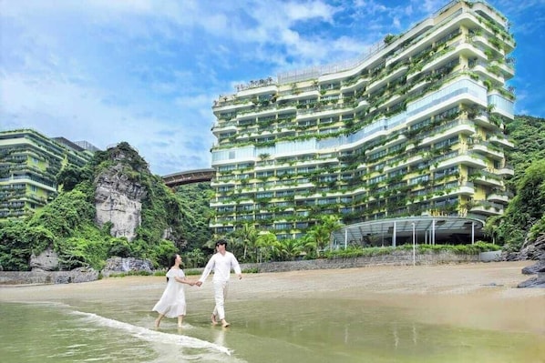 A multi-story hotel with balconies, a beach in the foreground, and greenery around. - Forest Sky Villa - Flamingo Cat Ba (Hai Phong)