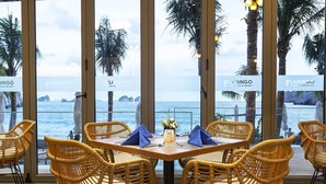 A dining area with wicker chairs and a table set for two, overlooking the sea. - Forest Sky Villa - Flamingo Cat Ba (Hai Phong)