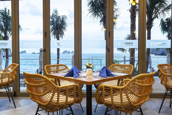 A dining area with wicker chairs and a table set for two, overlooking the sea. - Forest Sky Villa - Flamingo Cat Ba (Hai Phong)