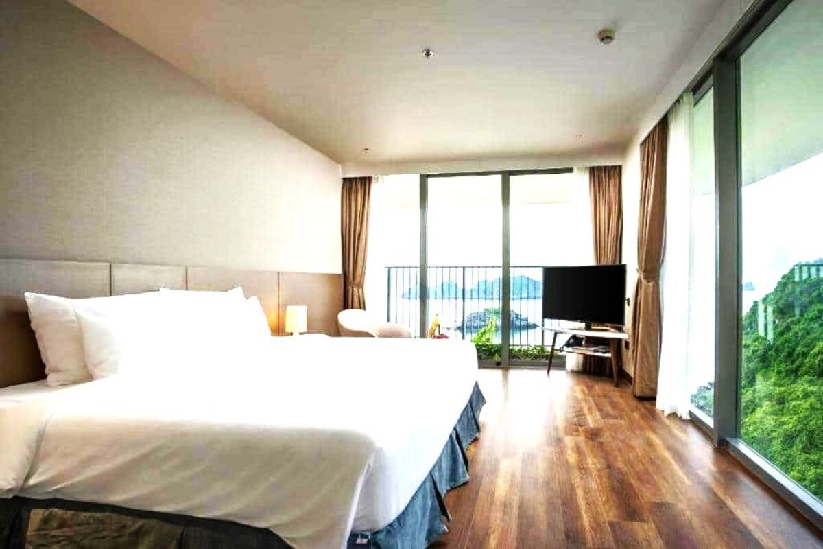 A hotel room with a large bed, a TV, a balcony with a view, and a wooden floor.
