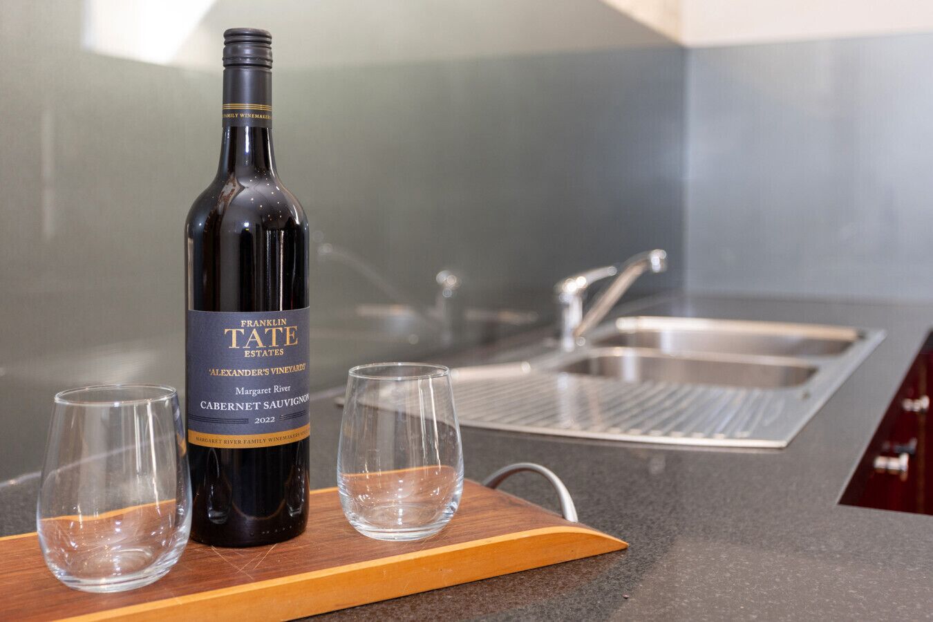 A bottle of Franklin Estate Cabernet Sauvignon on a wooden board with two glasses beside it in a modern kitchen setting.