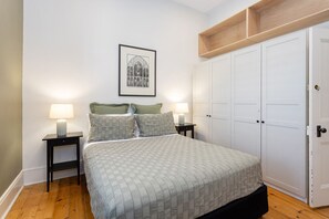 A bedroom with a bed, two bedside tables with lamps, a framed picture on the wall, and a wardrobe.