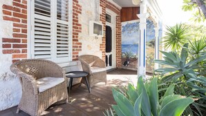 A brick house with a porch, two wicker chairs, a small table, and a painting of a cat. - Blue Door on Douglas - Fremantle Heritage Cottage (Fremantle)
