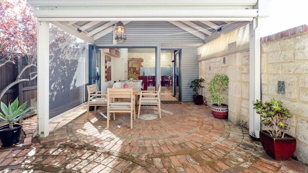A covered patio area with a brick floor, wooden furniture, and potted plants. - Blue Door on Douglas - Fremantle Heritage Cottage (Fremantle)